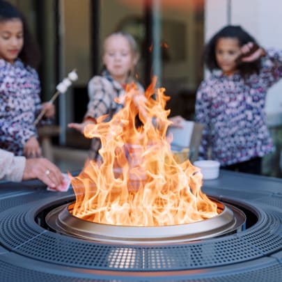 Children roasting marshmallows over a Solo Stove fire pit with flames and a blurred background